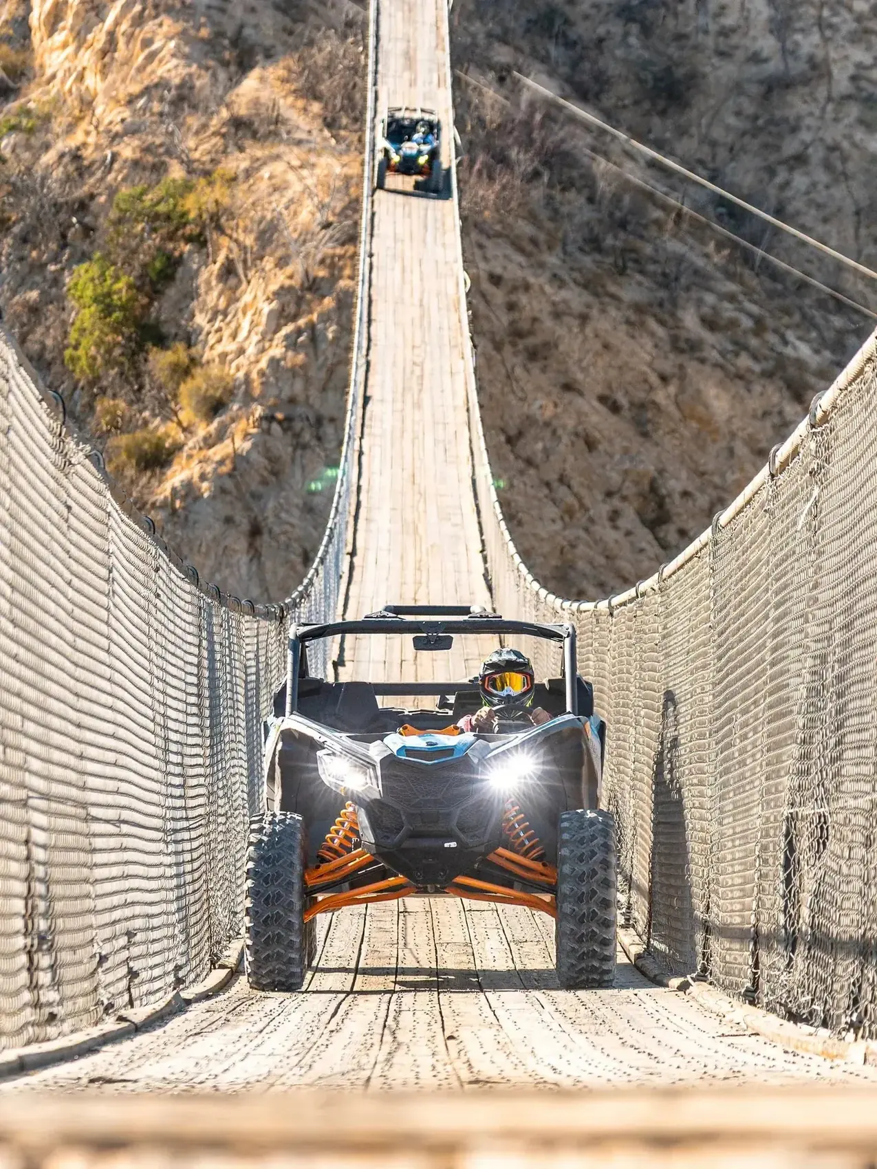 Dos Can-Am UTV con faros encendidos cruzando el puente colgante en convoy