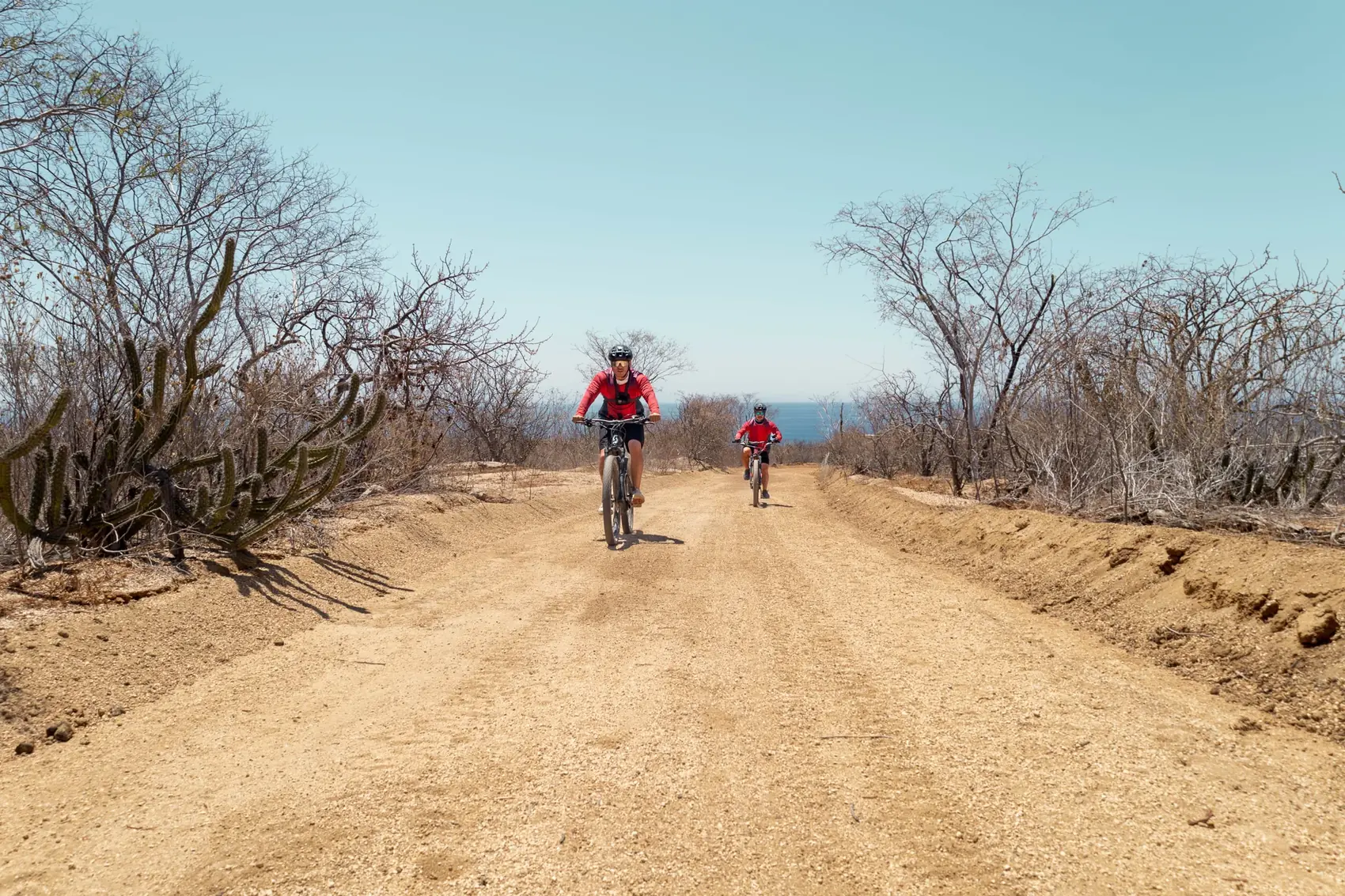 Dos riders en sendero de tierra con el oceano de fondo
