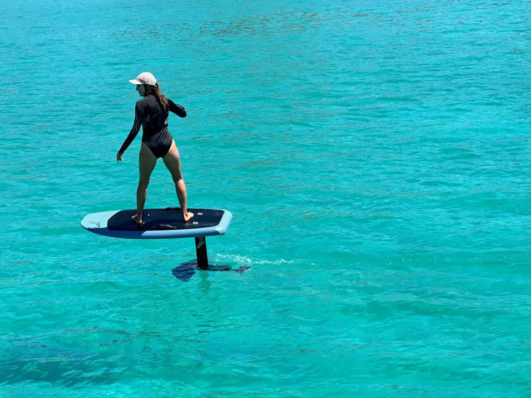 Mujer volando sobre el agua turquesa en una tabla e-foil