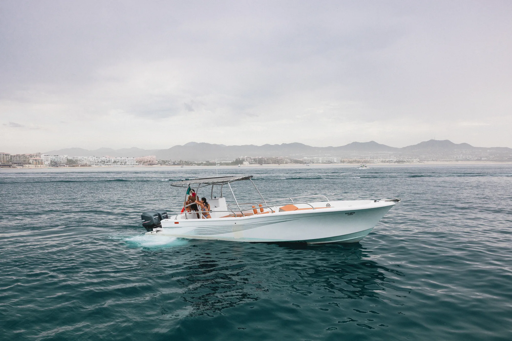 Barco de expedición blanco sobre agua en calma frente a Cabo San Lucas