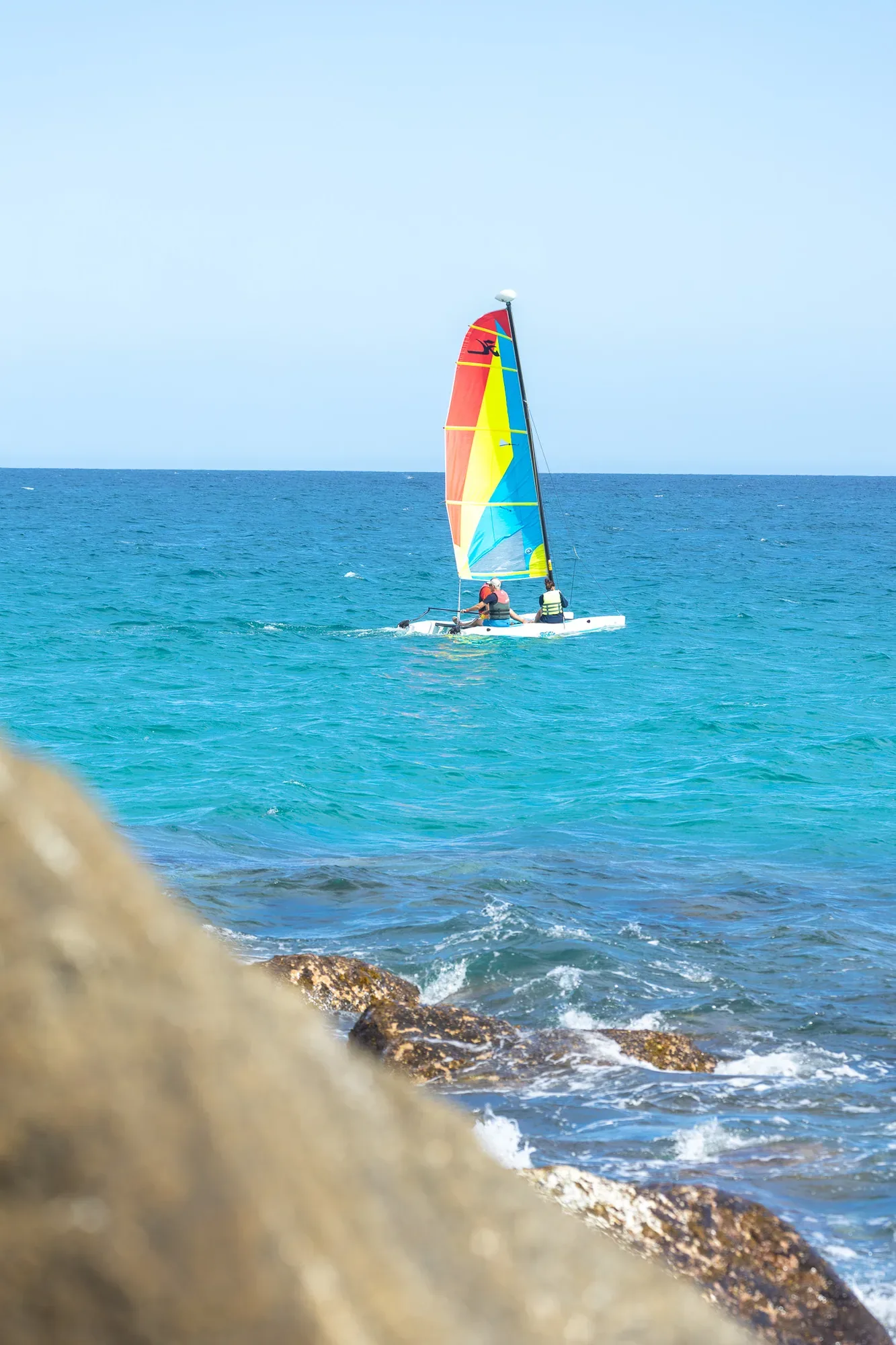 Hobie Cat de vela colorida navegando frente a la costa rocosa