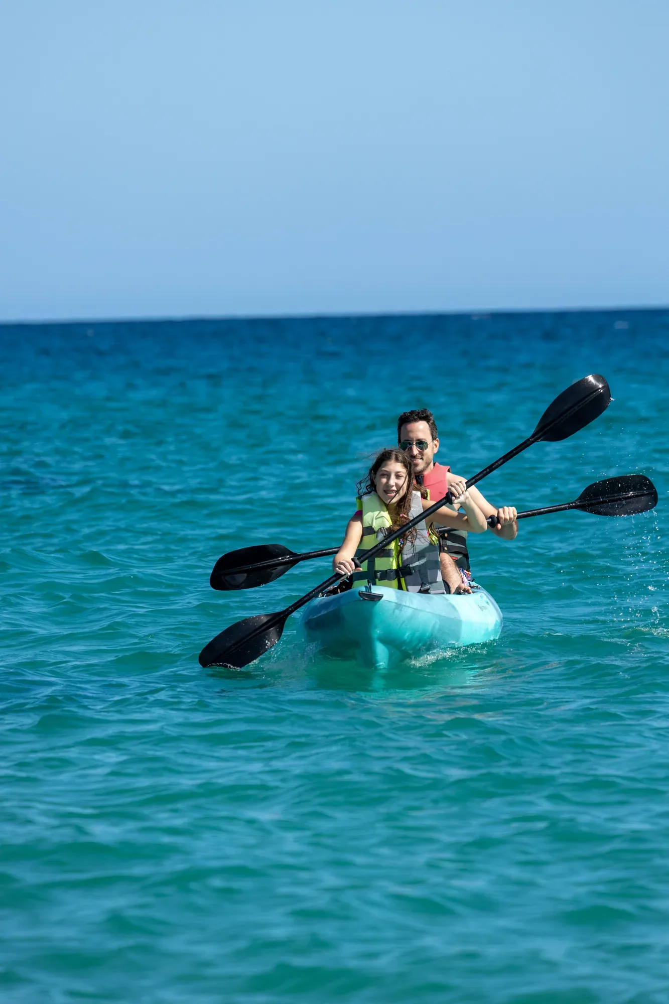 Hombre y nina en kayak doble sobre mar turquesa en Wild Bay
