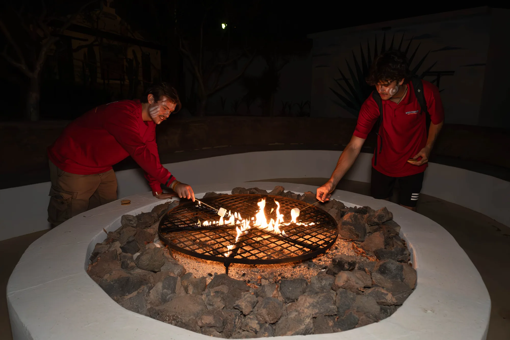 Dos miembros del staff asando malvaviscos en la fogata de noche