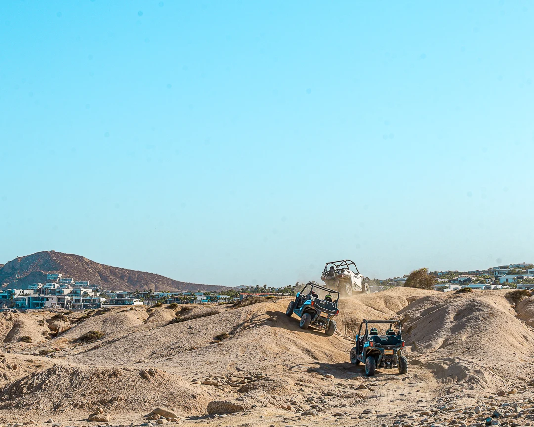 Tres UTV cruzando dunas con la ciudad de fondo